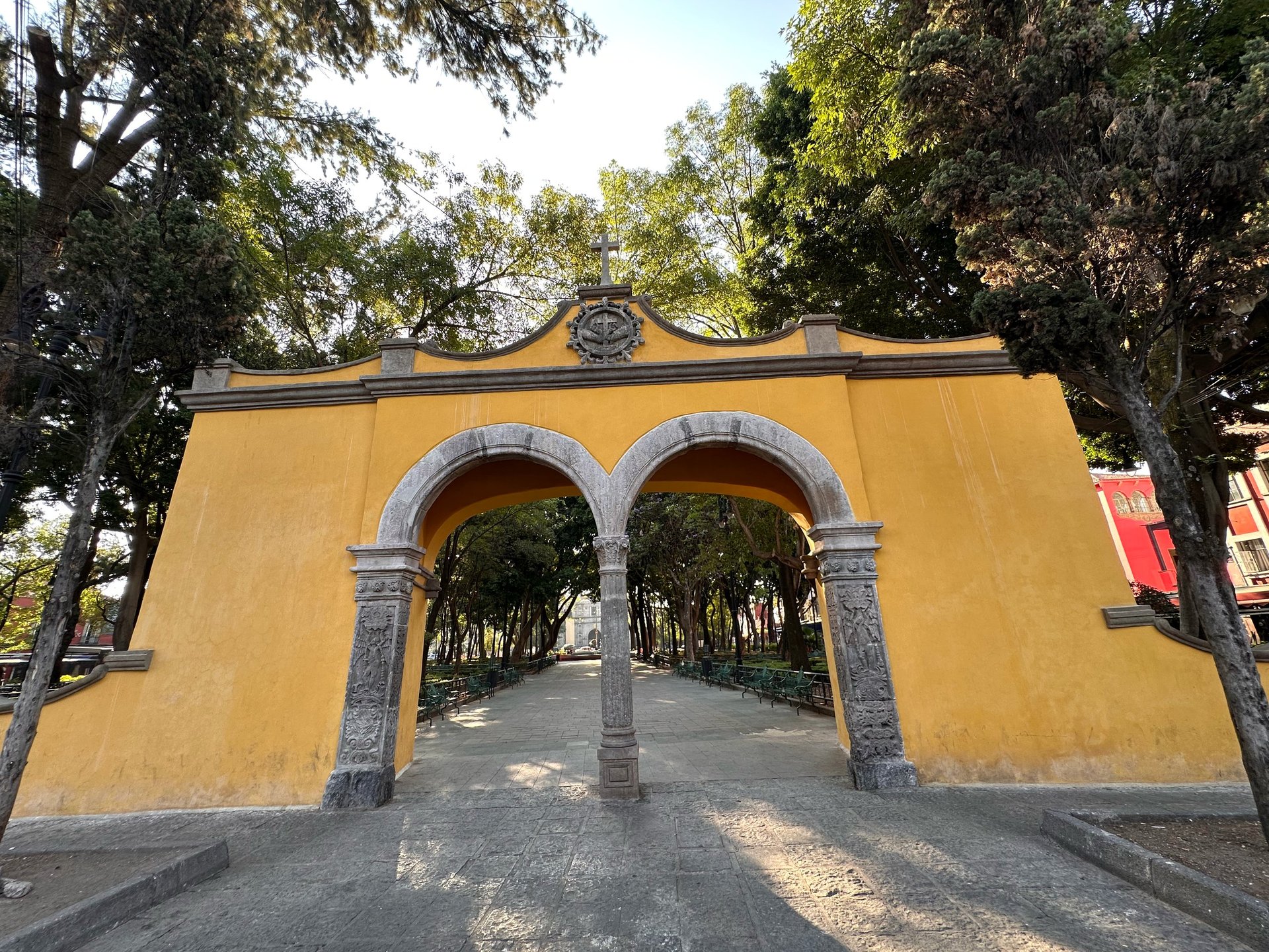 Yellow arched gateway entrance with gray stone pillars leading to tree-lined pathway