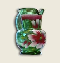 Decorative glass pitcher with green and red floral design on cream background